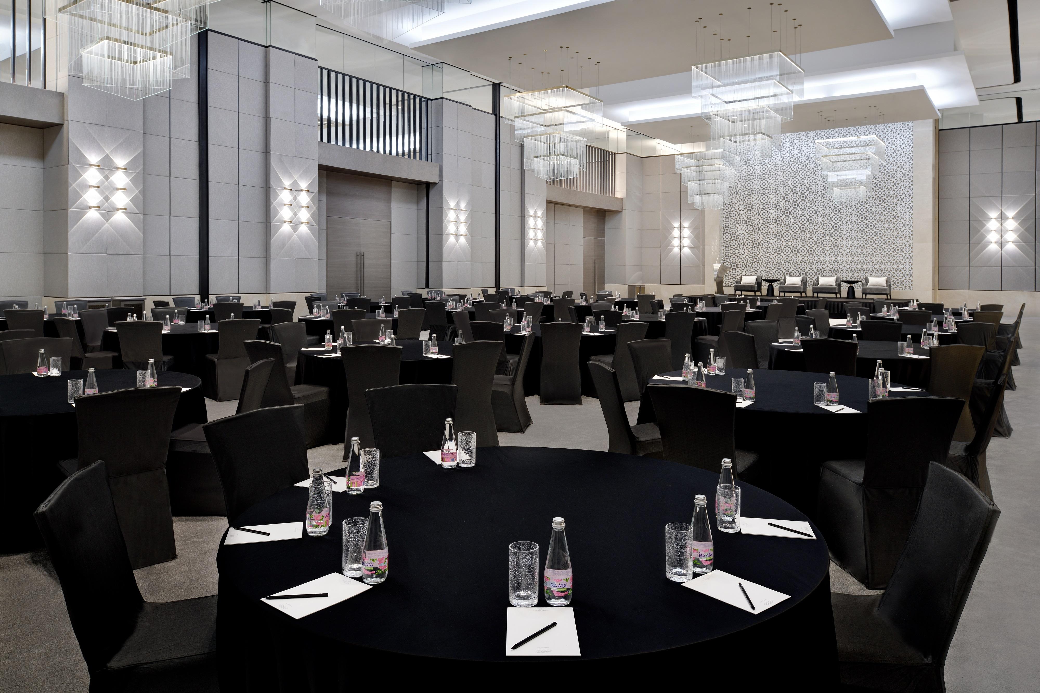 Kempinski Central Avenue Dubai Hotel Buitenkant foto The photo shows a spacious, elegantly designed banquet or conference hall. There are multiple round tables covered with black tablecloths, each set with glasses of water and paper notepads. The chairs are sleek and black, creating a modern look. The 