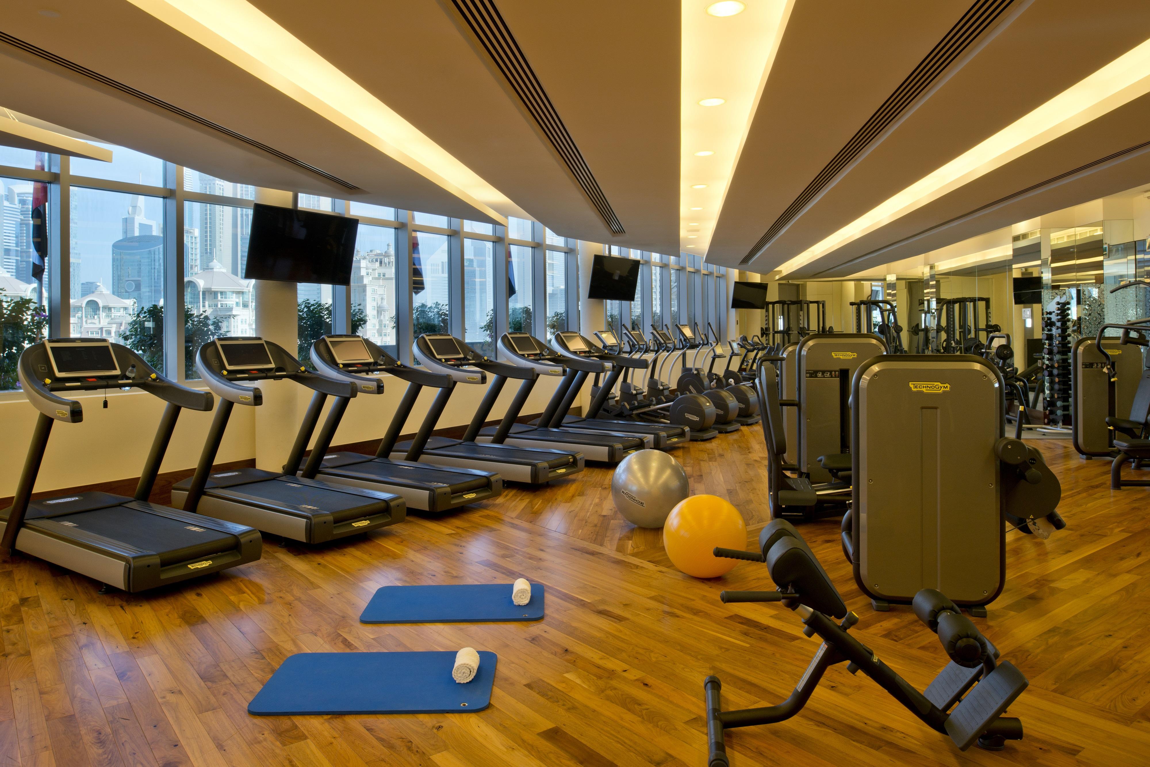 Kempinski Central Avenue Dubai Hotel Buitenkant foto The photo shows a modern gym interior with large windows allowing natural light to fill the space. There are several treadmills lined up against one wall, each equipped with screens. There are also various pieces of weight training equipment, includi