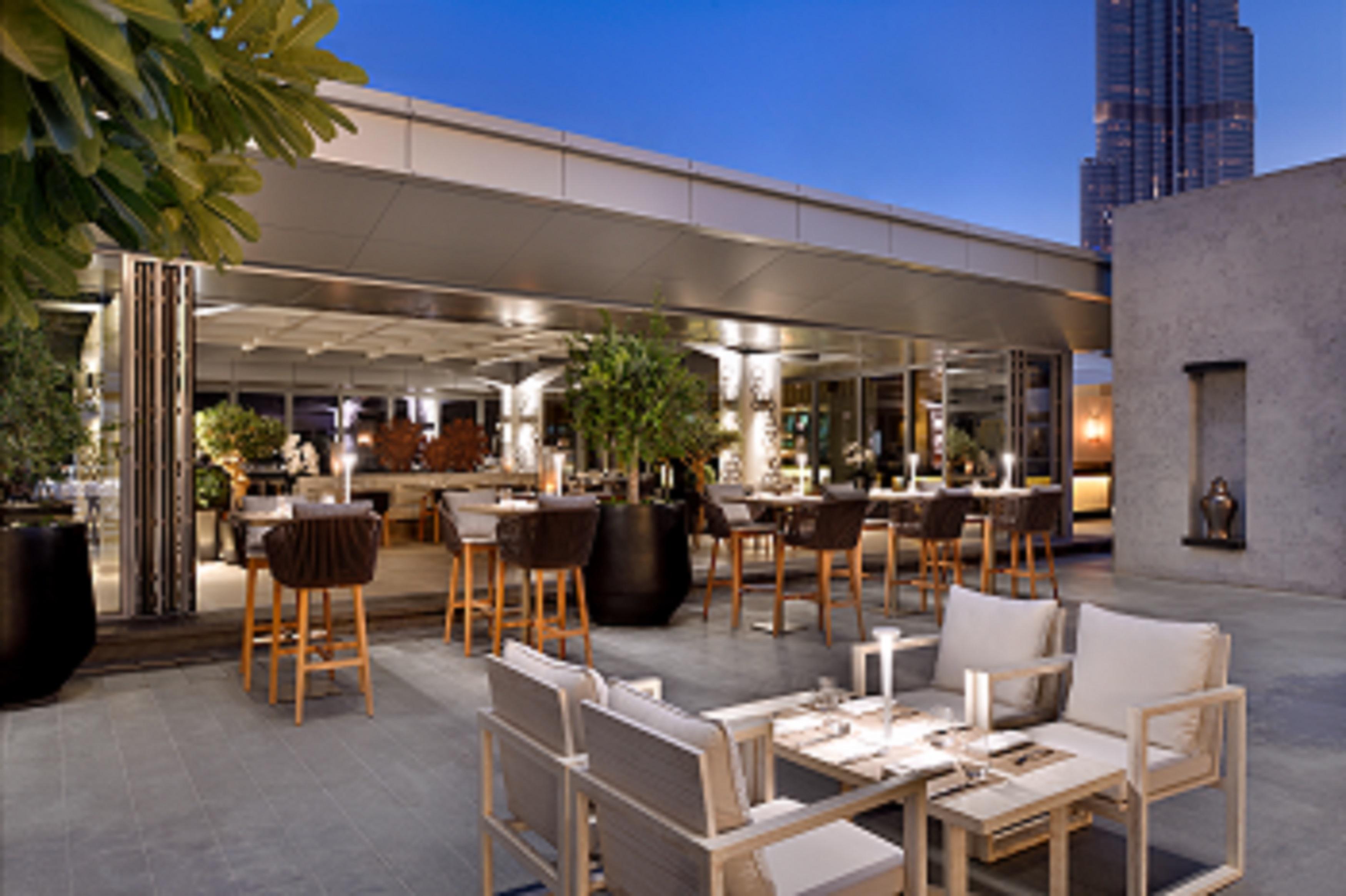 Kempinski Central Avenue Dubai Hotel Buitenkant foto The photo depicts a stylish rooftop dining area. There are several tall bar stools around a high table, and the space is adorned with modern furnishings and plants. Soft lighting enhances the ambiance, creating a warm and inviting atmosphere. In the 